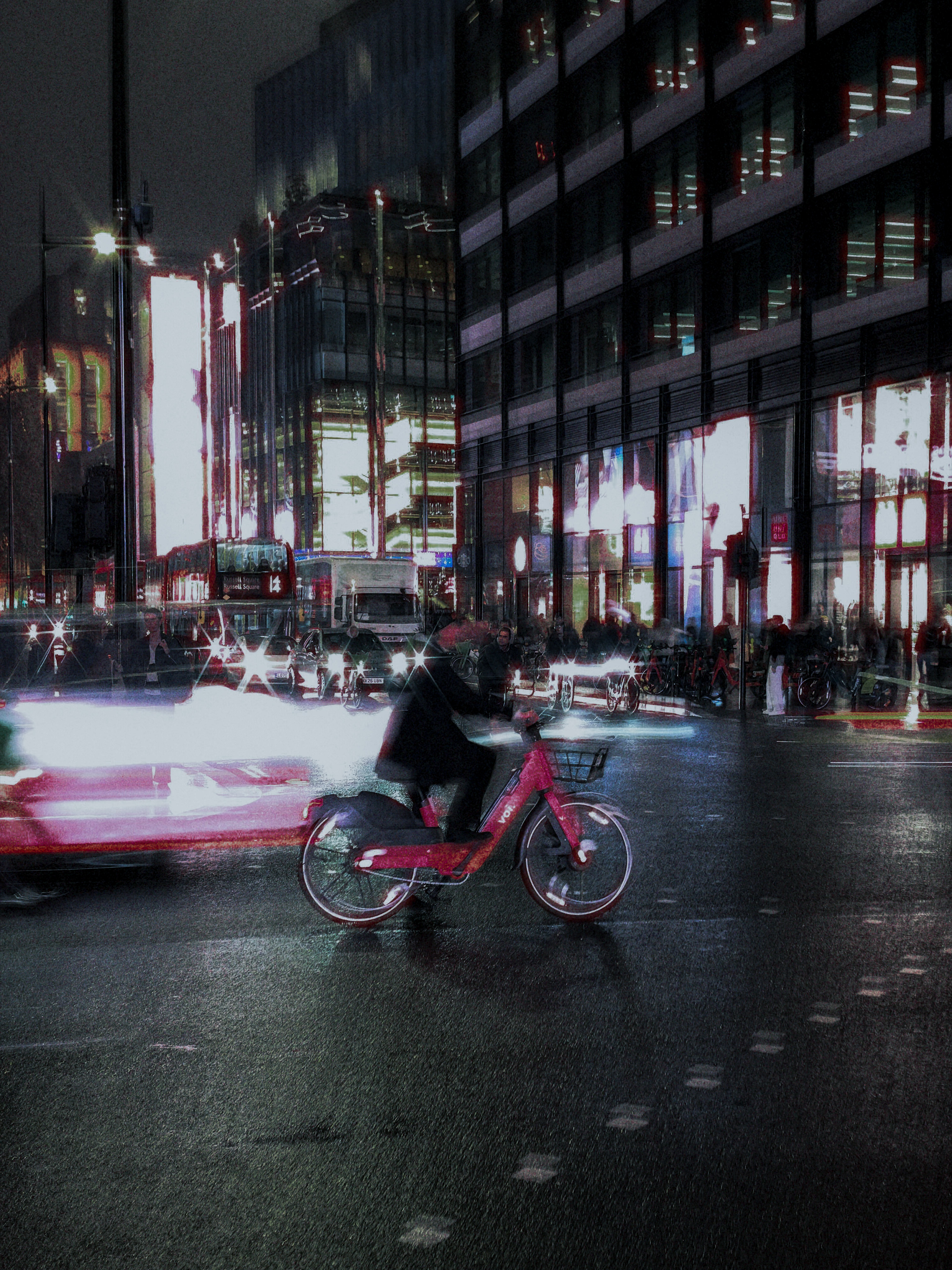 A cyclist on a pink bicycle crossing a wet London street amid blurred headlights